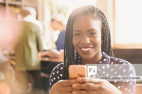 Porträt einer lächelnden afrikanischen Frau  die in einem Café eine SMS mit ihrem Handy schreibt