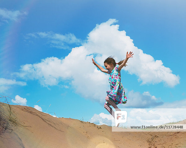 Überschwängliches Mädchen springt vor Freude am Strand Hügel unter sonnigen blauen Himmel mit Wolken