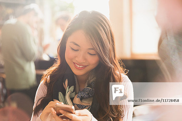 Lächelnde chinesische Frau  die in einem Café mit ihrem Handy SMS schreibt