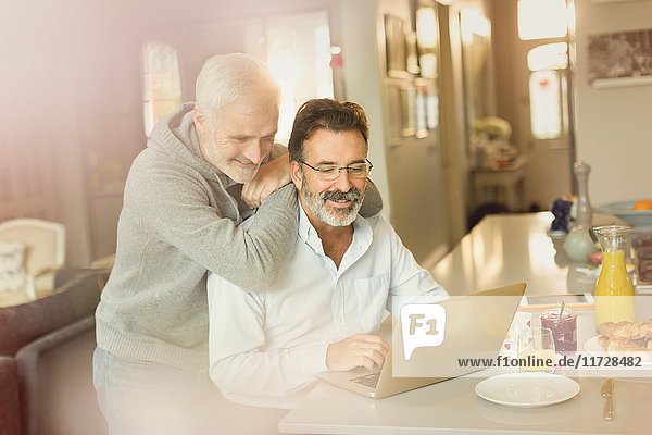 Männliches schwules Paar mit Laptop an der Frühstücksküche