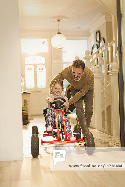 Vater schiebt Tochter auf Spielzeugauto im Foyerflur