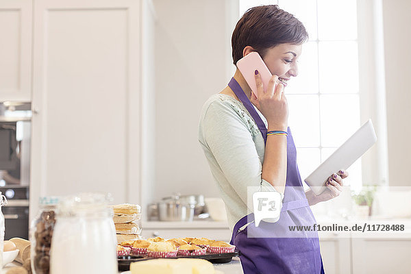Weibliche Caterer backen  telefonieren und digitales Tablett in der Küche benutzen