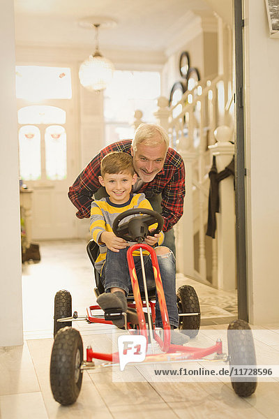 Vater schiebt Sohn auf Spielzeugauto im Foyerflur