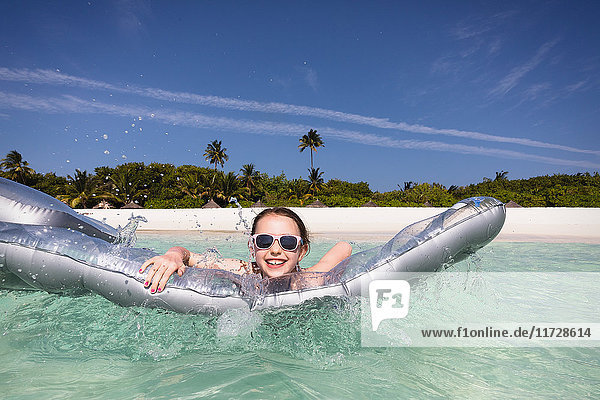 Portrait lächelndes Mädchen spielt mit aufblasbarem Floß im sonnigen tropischen Ozean