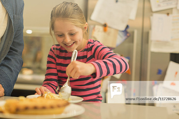 Lächelndes  eifriges Mädchen  das Kuchen in der Küche serviert.