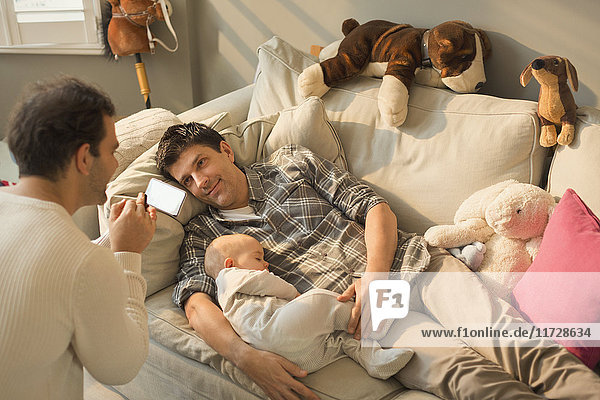 Male gay parents and baby son resting on living room sofa