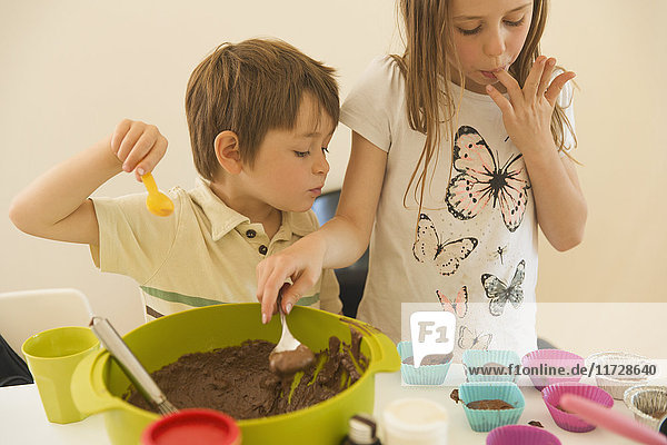 Junge und Mädchen  Bruder und Schwester  machen Schokoladen-Cupcakes  lecken sich die Finger