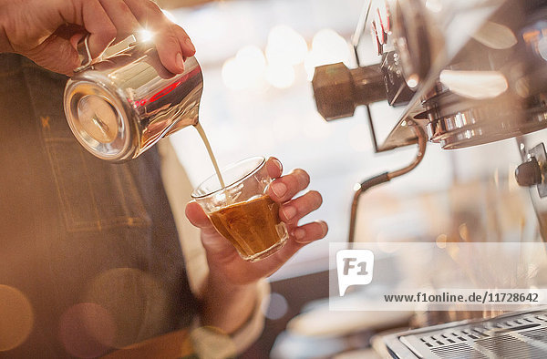 Nahaufnahme Barista gießt Milch in Espresso an Espressomaschine in Café