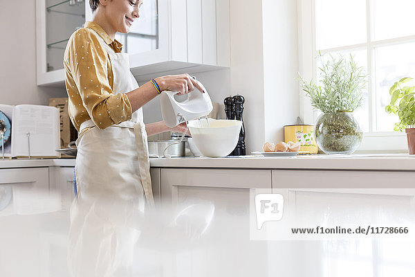 Woman baking  using electric hand mixer in kitchen