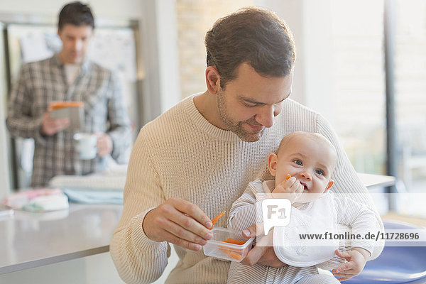 Father feeding carrots to baby son