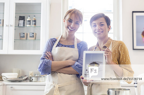Portrait confident female caterers showing food photograph on digital tablet in kitchen