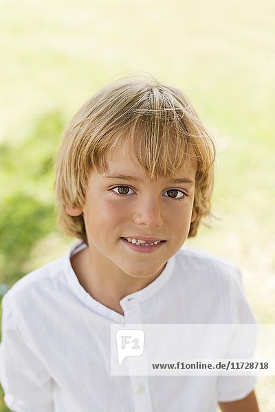 Portrait of a cute blond boy in park smiling at camera