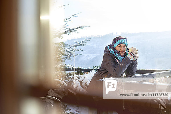 Portrait smiling female skier drinking hot cocoa on sunny cabin balcony