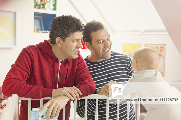 Male gay parents watching baby son in crib