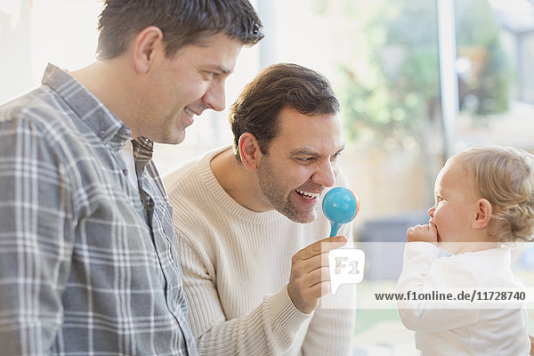 Male gay parents and baby son playing with rattle