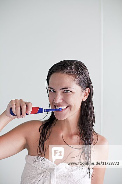 Brünette Frau beim Zähneputzen mit Blick auf die Kamera