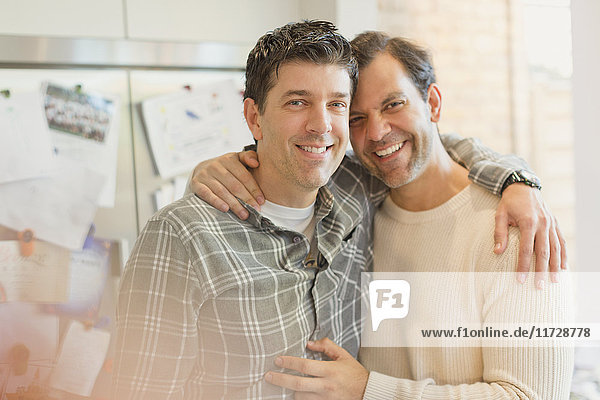 Porträt lächelndes  liebevolles männliches schwules Paar  das sich in der Küche umarmt.