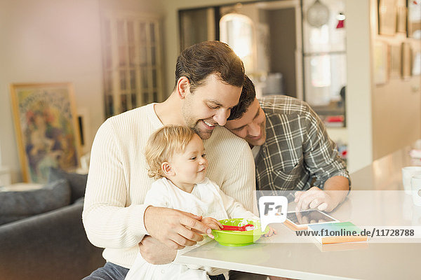 Männliche schwule Eltern  die ihren Sohn füttern und ein digitales Tablett benutzen.