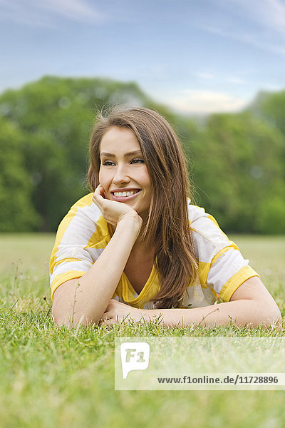 Porträt einer brünetten Frau im Park liegend  lächelnd und nachdenklich