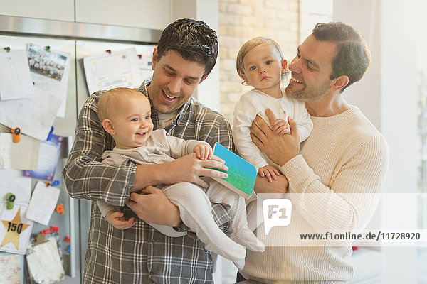 Male gay parents holding baby sons in kitchen