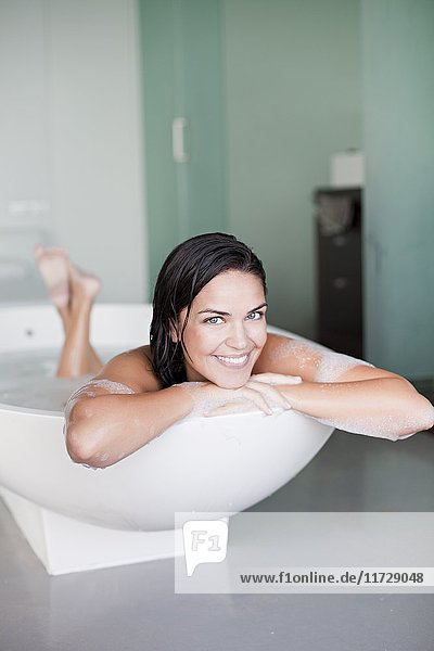 Junge hübsche brünette Frau genießt ein Bad und lächelt in die Kamera.