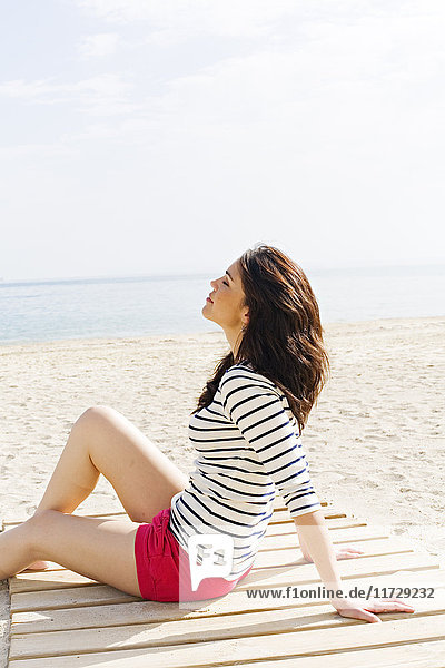 Porträt einer schönen brünetten Frau  die am Strand sitzt