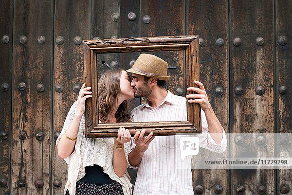 Portrait of couple  kissing  holding wooden frame in front of their faces  Mexico City  Mexico