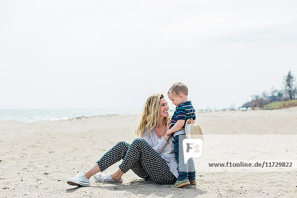 Young woman sitting on beach playing with toddler son