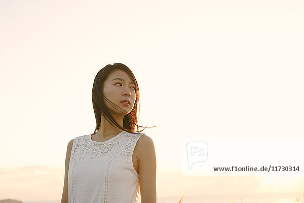 Junge Japanerin in einem weißen Kleid an einer Klippe über dem Meer bei Sonnenaufgang  Chiba  Japan