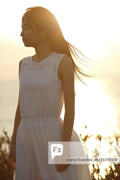 Young Japanese woman in a white dress at a cliff over the sea at sunrise  Chiba  Japan