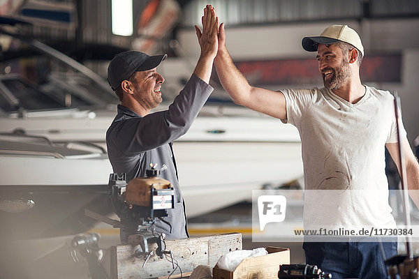 Two men high fiving in boat repair workshop