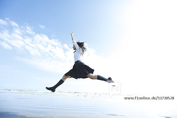 Young Japanese woman in a high school uniform jumping by the sea  Chiba  Japan