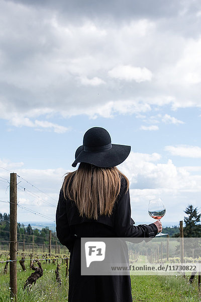 Frau steht im Weinberg  hält ein Glas Wein  Rückansicht