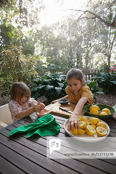Zwei junge Schwestern bereiten am Gartentisch Zitronen für Limonade zu