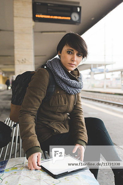 Porträt einer Rucksacktouristin mit Karte und digitalem Tablett auf dem Bahnsteig