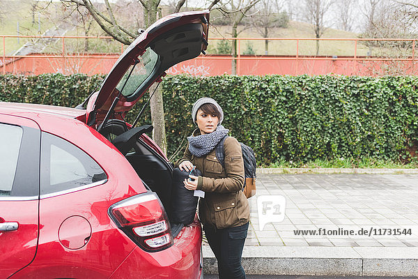 Female backpacker removing sleeping bag from car boot in city