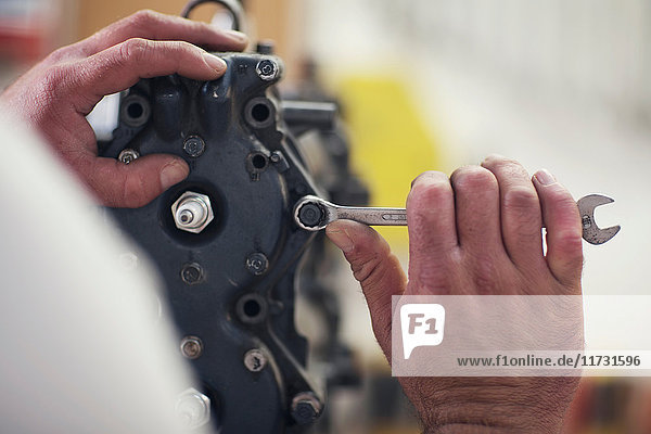 Nahaufnahme von männlichen Händen bei der Reparatur eines Außenbordmotors in einer Bootsreparaturwerkstatt