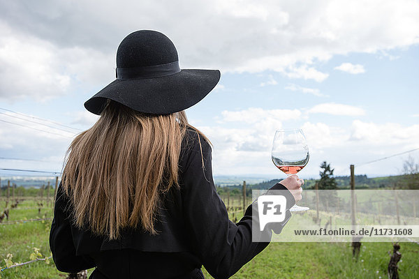 Frau steht im Weinberg  hält ein Glas Wein  Rückansicht