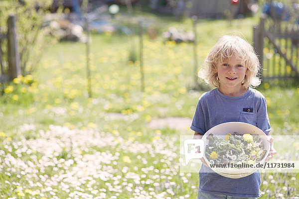 Porträt eines Jungen  der eine Schale mit Gartenkräutern hält