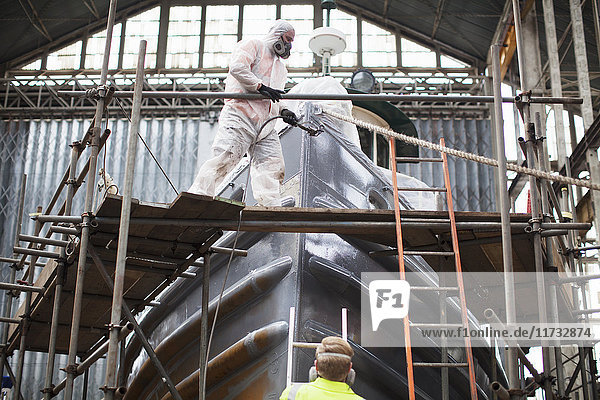 Workers spray-painting boat in shipyard