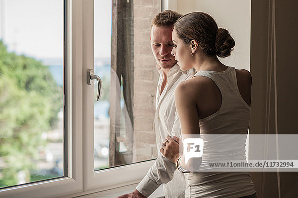 Junges Paar beim Plaudern und beim Blick aus dem Wohnzimmerfenster
