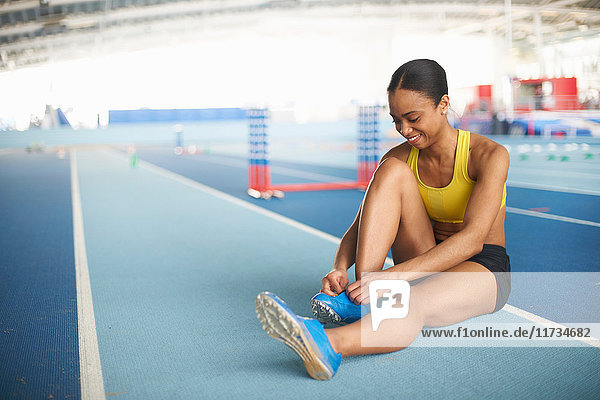 Junge Sportlerin sitzt auf dem Boden und bindet Schnürsenkel
