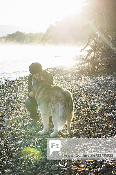 Woman crouching on bank of Bitterroot River stroking dog smiling  Missoula  Montana  USA