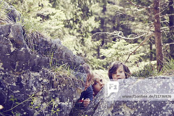 Drei Kinder verstecken sich hinter Felsen im Wald