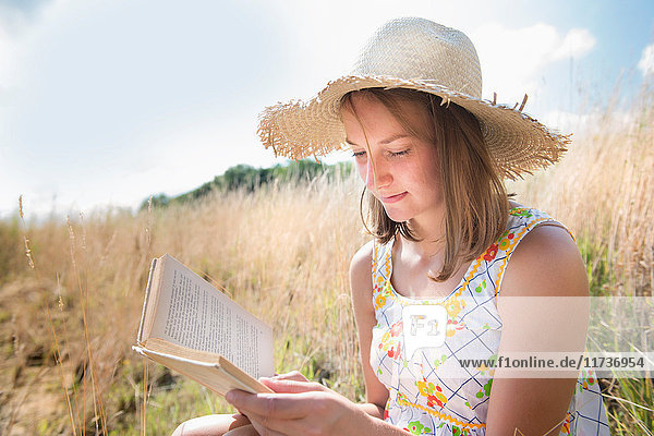 Heranwachsendes Mädchen sitzt im sonnenlesenden Geschichtenbuch