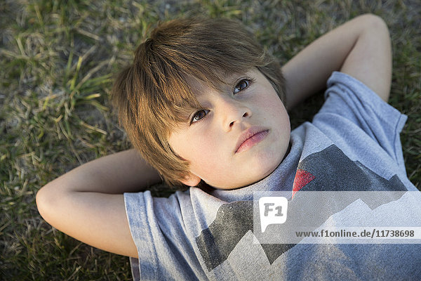 Portrait of boy lying on park grass gazing up