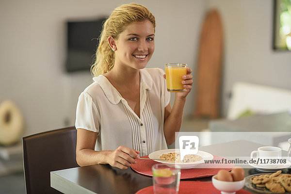 Junge Frau am Frühstückstisch trinkt Orangensaft