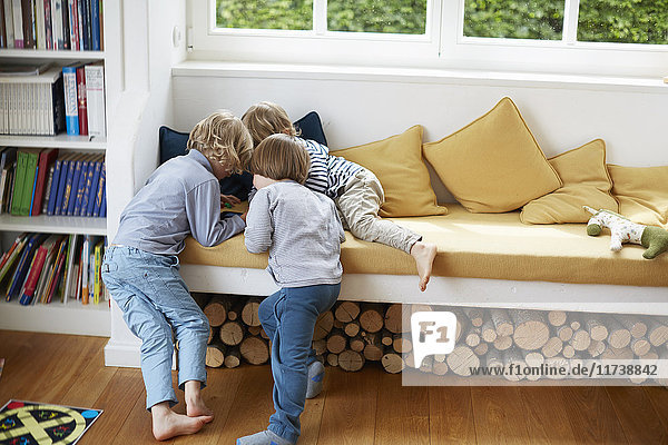 Three boys in a huddle on window seat playing