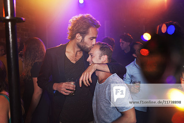 Junger Mann küsst im Club den Kopf eines Freundes