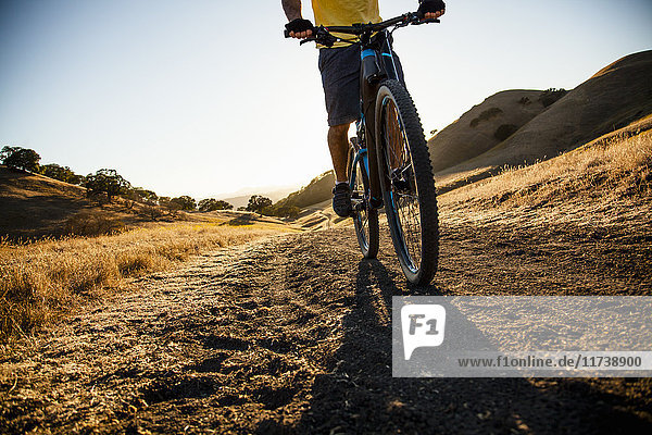 Silhouetted cropped view of young man mountain biking down dirt track  Mount Diablo  Bay Area  California  USA